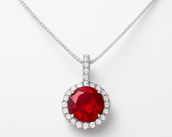 May include: A silver necklace with a round pendant. The pendant has a large, deep red gemstone encircled by smaller, clear stones. The necklace hangs from a delicate chain, offering a classic and elegant appearance.