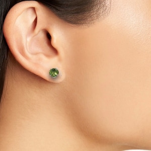 May include: A pair of green gemstone stud earrings. The earrings are set in a silver metal setting.