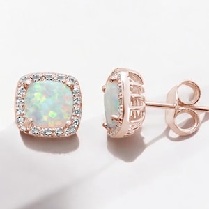 Pode incluir: Um par de brincos de ouro rosa com uma pedra de opala quadrada cercada por um halo de pedras menores transparentes.