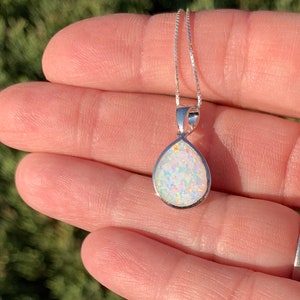 May include: A silver teardrop-shaped pendant necklace with a white opal gemstone. The opal has a rainbow iridescent sheen.