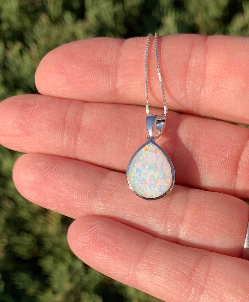 May include: A silver teardrop-shaped pendant necklace with a white opal gemstone. The opal has a rainbow iridescent sheen.