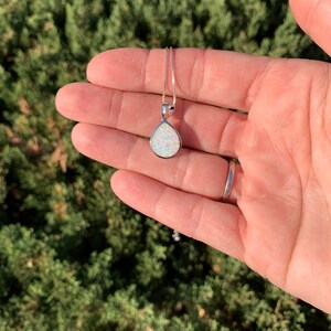 May include: A silver chain necklace with a teardrop-shaped white opal pendant.