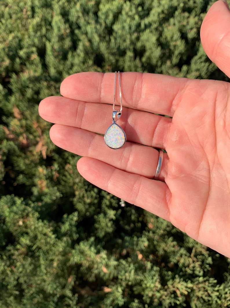 May include: A silver chain necklace with a teardrop-shaped white opal pendant.