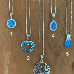 May include: Five silver necklaces with different opal pendants. The pendants include a round opal with a halo of smaller stones, a heart-shaped opal, a tree of life design, a teardrop-shaped opal, and a round opal with a crown.