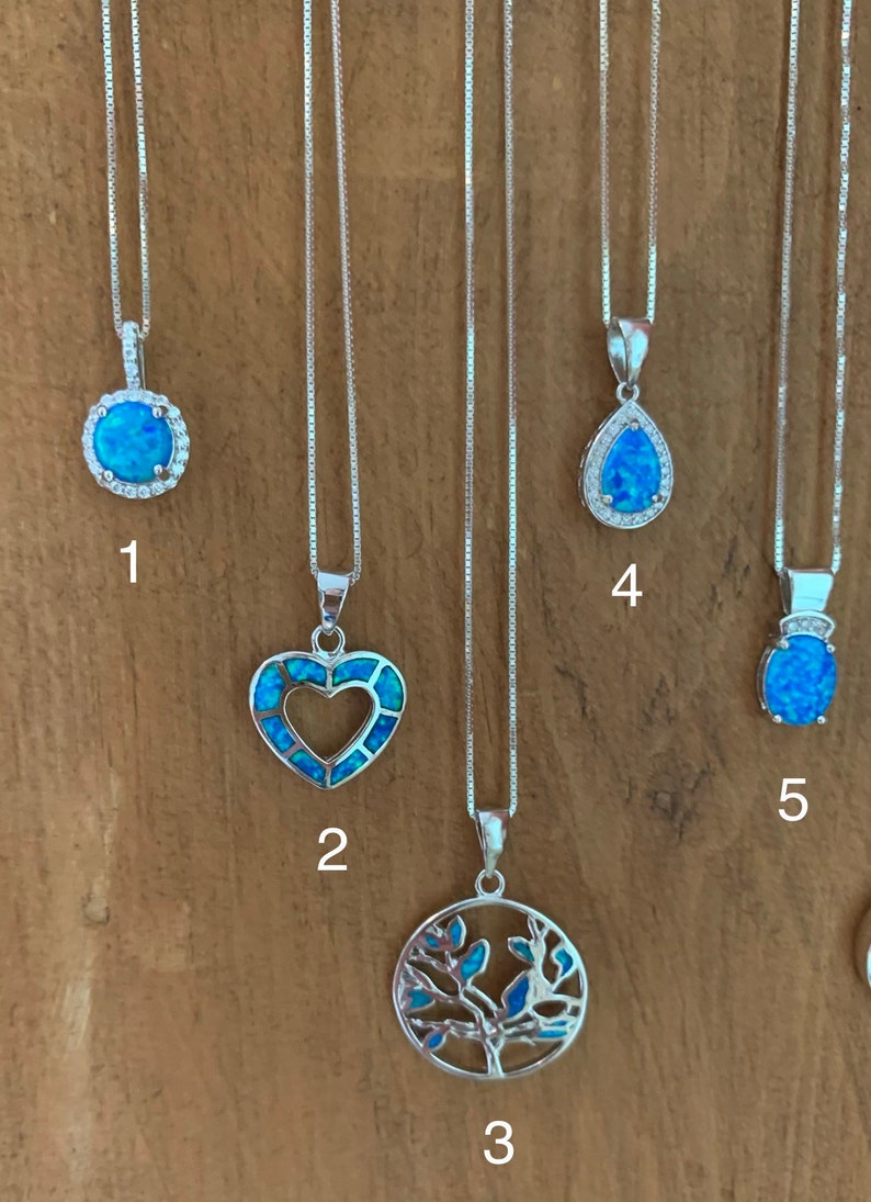 May include: Five silver necklaces with different opal pendants. The pendants include a round opal with a halo of smaller stones, a heart-shaped opal, a tree of life design, a teardrop-shaped opal, and a round opal with a crown.