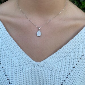 May include: A silver chain necklace with a teardrop-shaped pendant featuring a white opal stone.