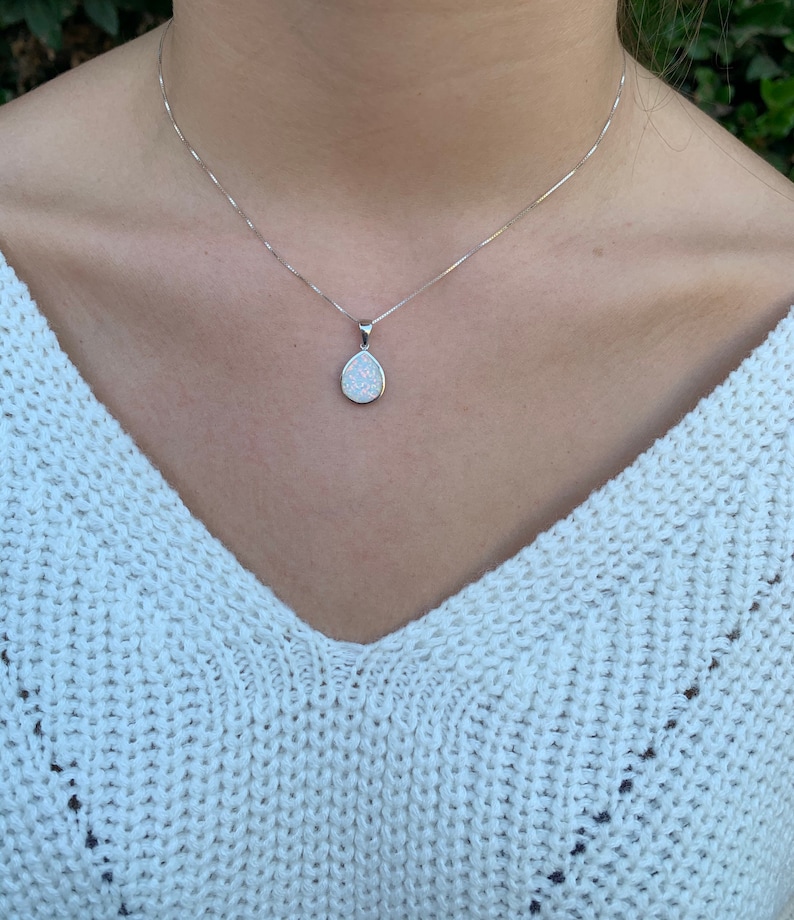 May include: A silver chain necklace with a teardrop-shaped pendant featuring a white opal stone.