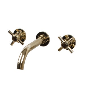 Puede incluir: Un grifo de ba&ntilde;o de pared dorado con dos manijas en forma de cruz.