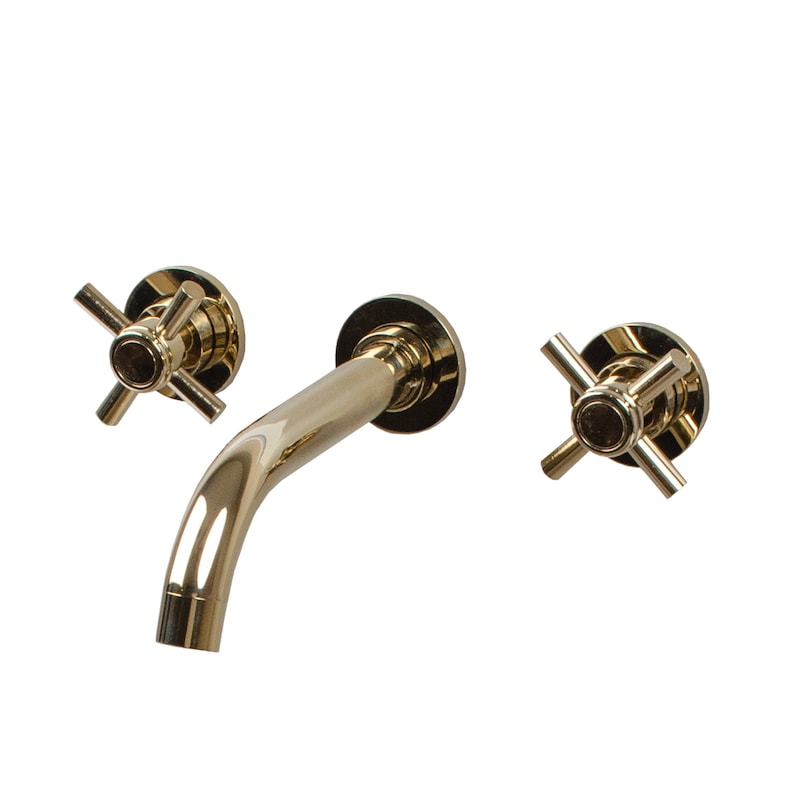 Puede incluir: Un grifo de ba&ntilde;o de pared dorado con dos manijas en forma de cruz.