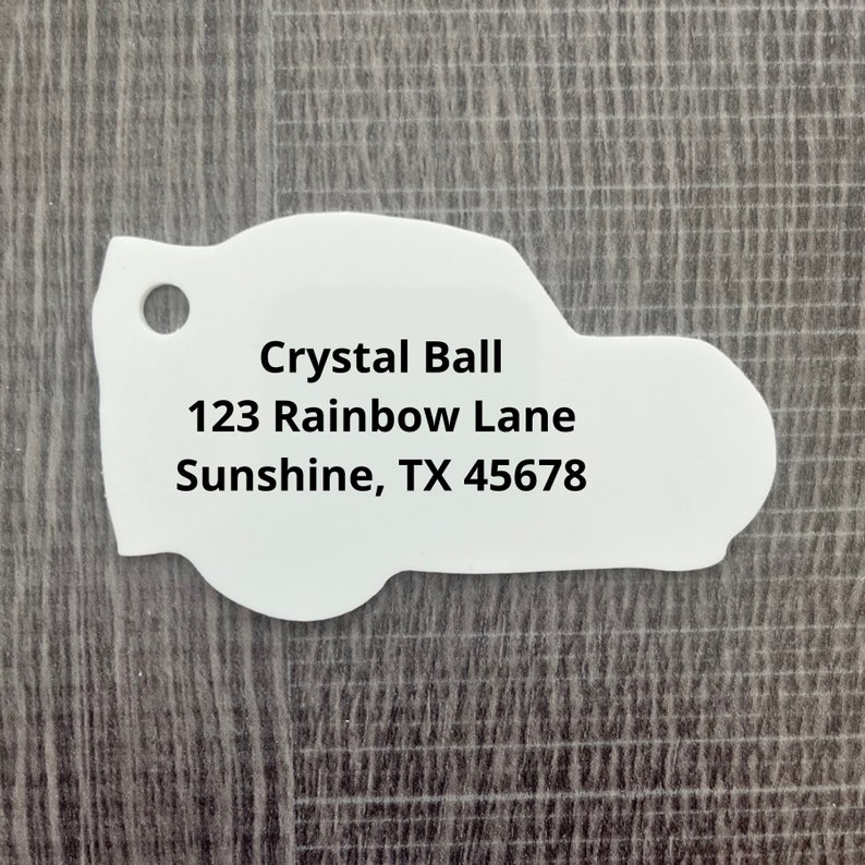 May include: White car-shaped tag with black text that reads "Crystal Ball 123 Rainbow Lane Sunshine, TX 45678"