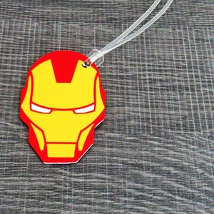 Puede incluir: Etiqueta de equipaje roja y amarilla con una imagen de dibujos animados de la cara de Iron Man.