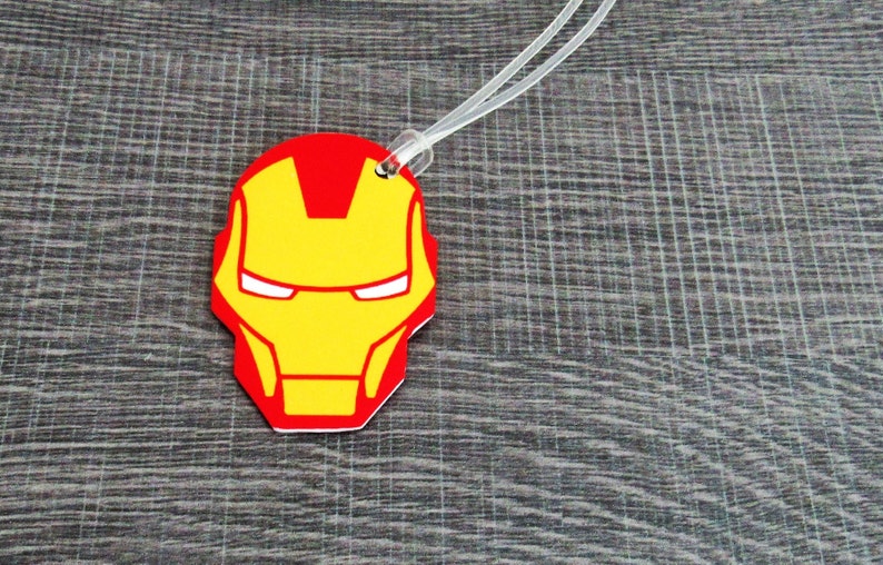 Puede incluir: Etiqueta de equipaje roja y amarilla con una imagen de dibujos animados de la cara de Iron Man.