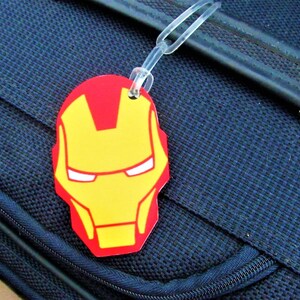 Puede incluir: Una etiqueta de equipaje roja y amarilla con una imagen de la cara de Iron Man.