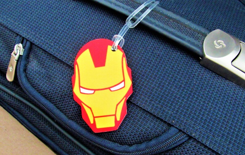 Puede incluir: Una etiqueta de equipaje roja y amarilla con una imagen de la cara de Iron Man.