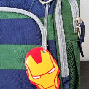 Puede incluir: Una mochila a rayas verde y azul con una etiqueta de equipaje de Iron Man de color rojo y amarillo.