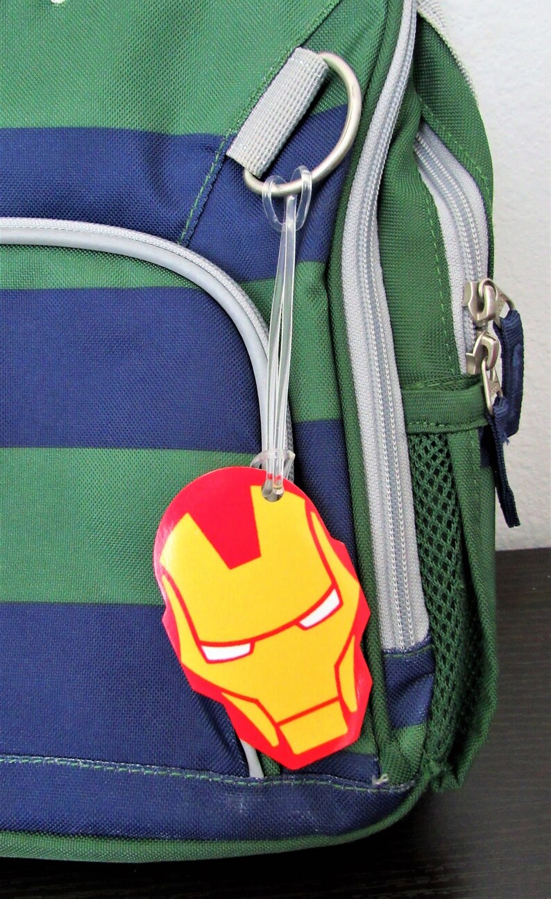 Puede incluir: Una mochila a rayas verde y azul con una etiqueta de equipaje de Iron Man de color rojo y amarillo.