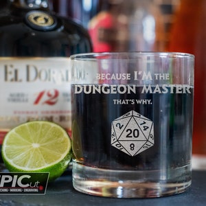 May include: A clear glass tumbler with the text "Because I'm the Dungeon Master That's Why." and a black and white image of a 20-sided die.