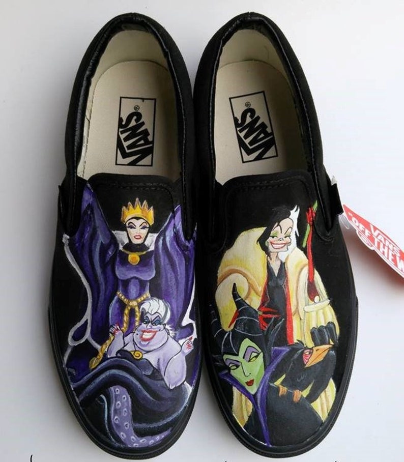 May include: Black slip-on Vans shoes with a hand-painted design featuring Disney villains: Maleficent, Ursula, Cruella de Vil, and the Evil Queen. The shoes have the Vans logo on the back.