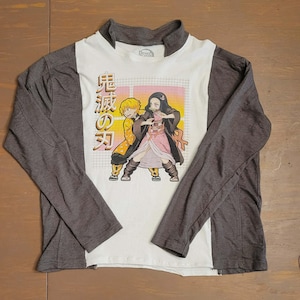 May include: A long-sleeved shirt featuring a graphic of two anime characters. The shirt has a white front panel with the graphic and gray sleeves and back. The characters are in a dynamic pose, with Japanese text on the left.