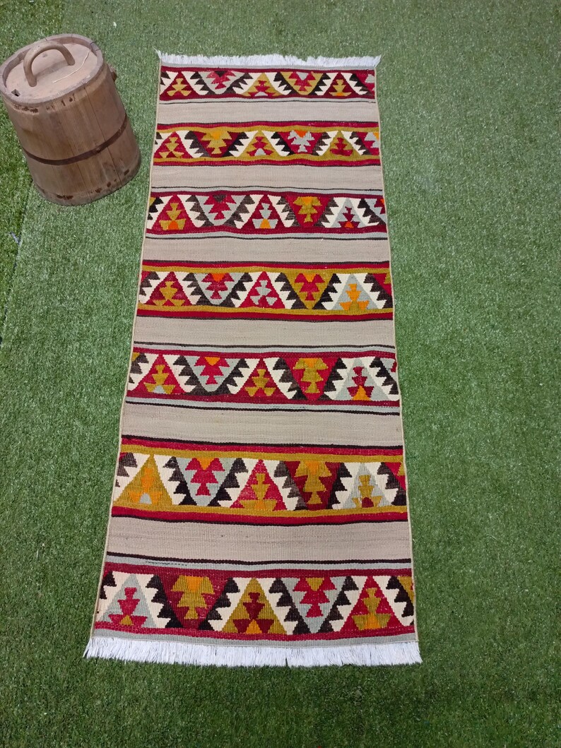 May include: A long, rectangular rug with a white fringe. The rug has a geometric pattern in shades of red, yellow, black, and gray.