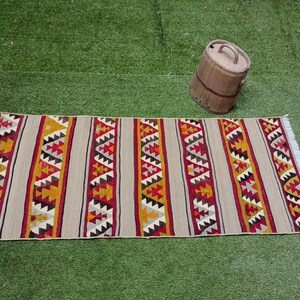 May include: A beige, red, and yellow patterned rug with a geometric design. The rug has a fringe on the ends.