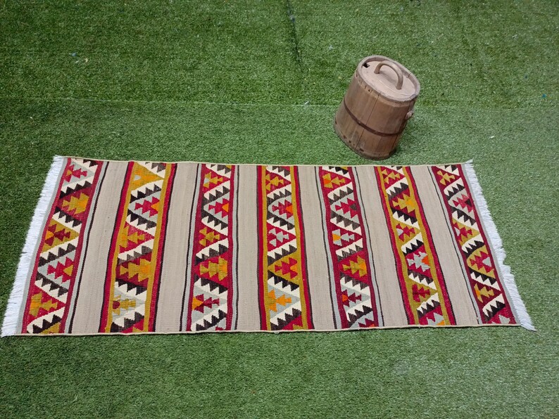 May include: A beige, red, and yellow patterned rug with a geometric design. The rug has a fringe on the ends.
