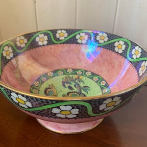 Op de afbeelding: Een decoratieve roze kom met een bloemmotief. De kom heeft een gouden rand en een voetstuk. De binnenkant heeft een groen en goudkleurig medaillon met een vlinder- en vogelontwerp. De rand is versierd met witte bloemen.
