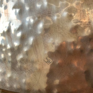 Pu&ograve; includere: Primo piano di un vassoio d'argento con un marchio a forma di diamante al centro. Il marchio contiene un uccello stilizzato con le ali spiegate.