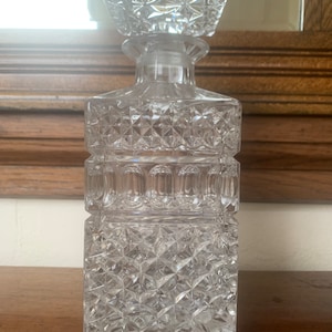 Puede incluir: Una decantador de vidrio transparente con un cuerpo cuadrado y un patrón en forma de diamante. El decantador tiene un tapón cuadrado con un patrón en forma de diamante.