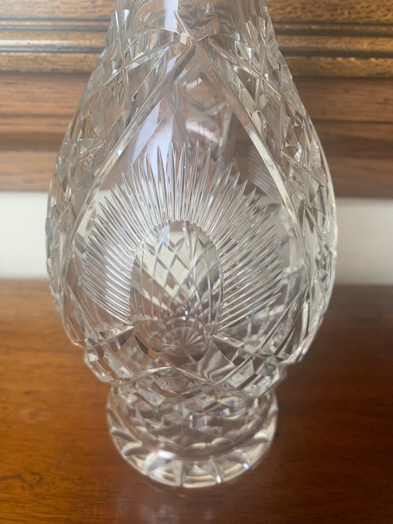 May include: A clear glass decanter with a cut crystal design. The decanter has a round body and a wide base.