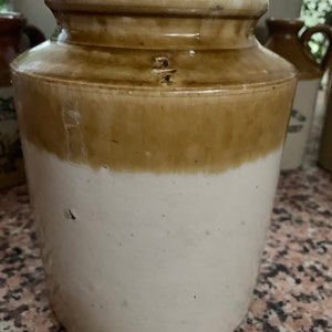 May include: A large, white and brown ceramic jar with a wide mouth. The jar has a glaze that is slightly uneven, giving it a rustic look.