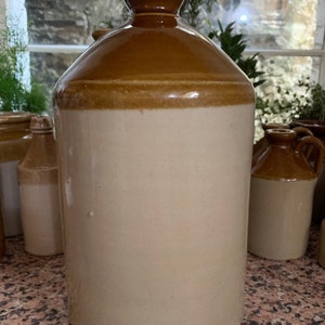 Può includere: Un grande vaso di ceramica marrone e bianco con un'ampia apertura e un tappo di sughero. Il vaso è smaltato e ha una superficie liscia leggermente ruvida.