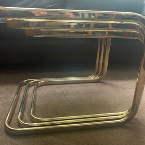 Puede incluir: Tres mesas nido de metal dorado con un diseño curvo. Las mesas están apiladas una encima de la otra.