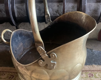 Può includere: Un secchio per carbone in ottone con un manico decorativo e una base scanalata. Il secchio è in condizioni usurate, mostrando segni di età e di utilizzo.