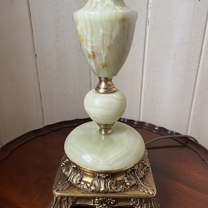 Peut inclure: Une lampe de table vintage avec un corps en onyx vert et des d&eacute;tails en laiton. La lampe a une base orn&eacute;e. Le corps de la lampe a une forme bulbeuse et un design classique, adapt&eacute; &agrave; un salon ou une chambre. La lampe mesure environ 40 cm de haut.