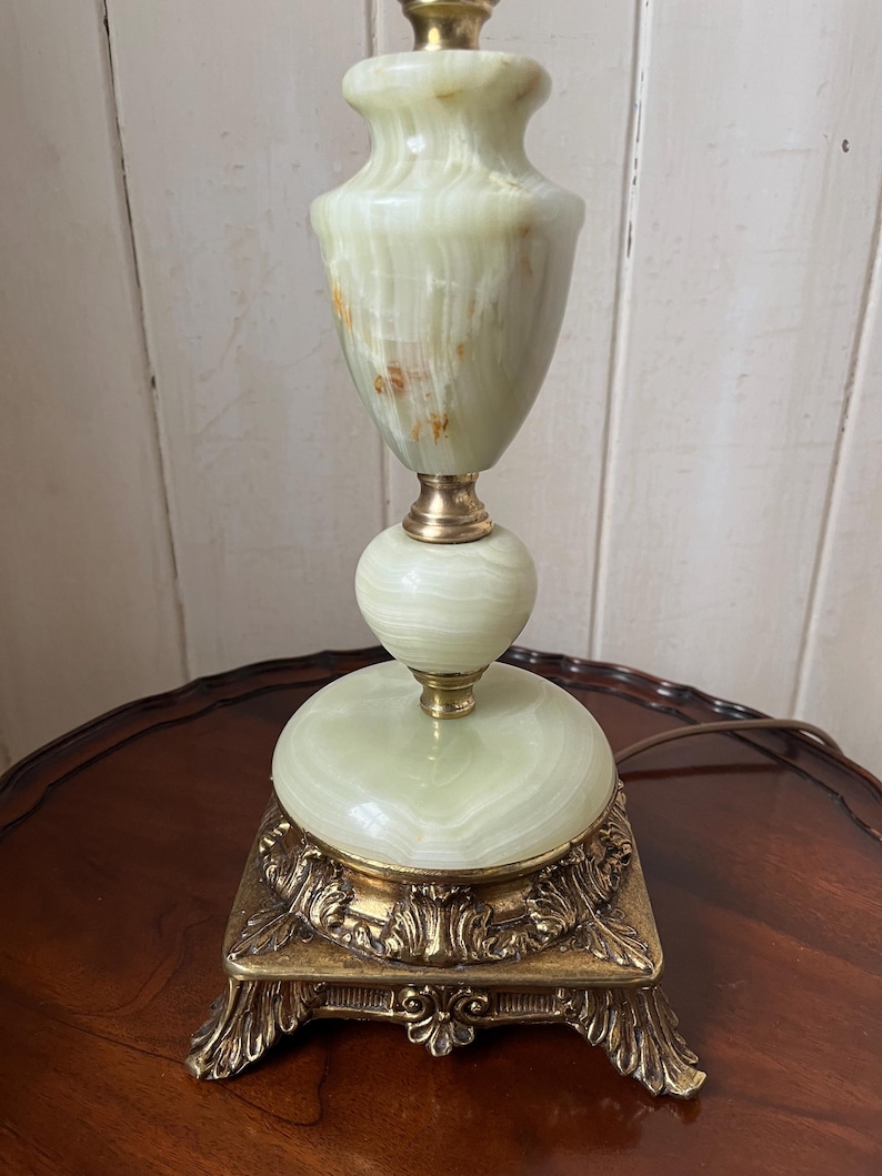 Peut inclure: Une lampe de table vintage avec un corps en onyx vert et des d&eacute;tails en laiton. La lampe a une base orn&eacute;e. Le corps de la lampe a une forme bulbeuse et un design classique, adapt&eacute; &agrave; un salon ou une chambre. La lampe mesure environ 40 cm de haut.