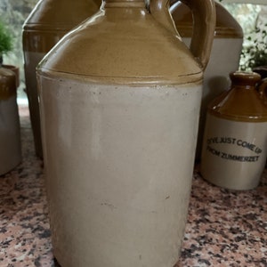 Può includere: Una brocca in ceramica marrone e bianca con un manico. La brocca ha la parte superiore marrone e quella inferiore bianca. La brocca ha il testo "Ive just come up from Zummerzet" sul lato.