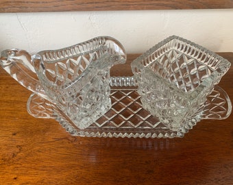 May include: A clear glass sugar and creamer set with a diamond pattern. The set includes a creamer, a sugar bowl, and a tray.