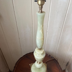 Peut inclure: Une lampe de table vintage avec un corps en onyx vert clair et des accents en laiton. La lampe a une base carr&eacute;e avec des d&eacute;tails orn&eacute;s et une douille en haut. La lampe mesure environ 51 cm de haut.