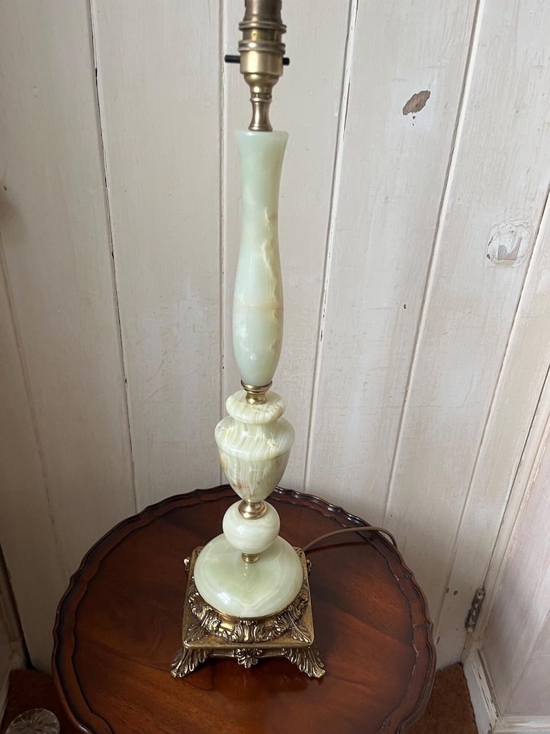Peut inclure: Une lampe de table vintage avec un corps en onyx vert clair et des accents en laiton. La lampe pr&eacute;sente une base carr&eacute;e avec des d&eacute;tails orn&eacute;s, une partie centrale renfl&eacute;e et une colonne &eacute;lanc&eacute;e. La lampe mesure environ 61 cm de haut.