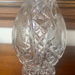 May include: A clear glass decanter with a cut crystal design. The decanter has a round body and a wide base.