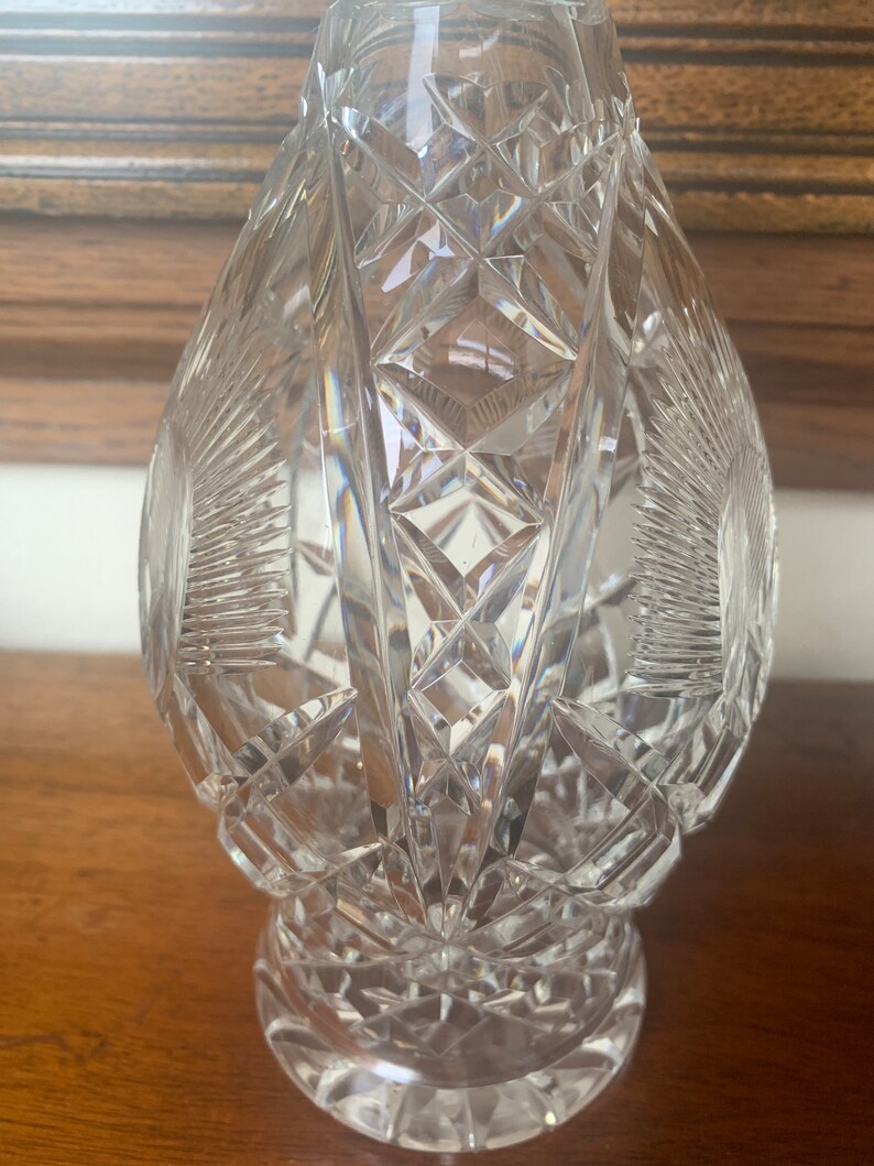 May include: A clear glass decanter with a cut crystal design. The decanter has a round body and a wide base.