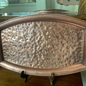 May include: A hammered copper serving tray with two handles. The tray is oval shaped and has a textured surface.