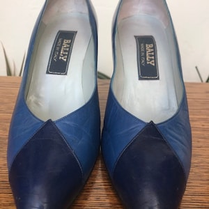 Può includere: Un paio di décolleté Bally in pelle blu con punta a punta. Le scarpe hanno un design bicolore con punta e tacco blu scuro. L'etichetta all'interno delle scarpe recita "Bally Made in Italy."