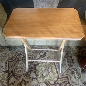 May include: A wooden folding table with a light brown finish. The table has a rectangular top and a simple, open frame.