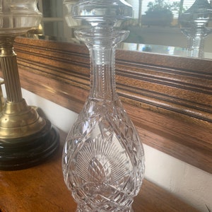 May include: A clear glass decanter with a cut crystal design. The decanter has a stopper with a pointed top.