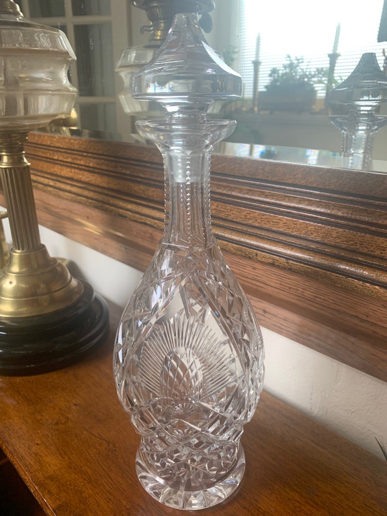 May include: A clear glass decanter with a cut crystal design. The decanter has a stopper with a pointed top.