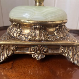 Peut inclure: Gros plan sur un pied de lampe vintage. La base est en m&eacute;tal dor&eacute; orn&eacute; de d&eacute;tails floraux et de volutes complexes. Le dessus pr&eacute;sente une pierre ovale vert clair.
