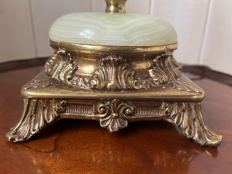 Peut inclure: Gros plan sur un pied de lampe vintage. La base est en m&eacute;tal dor&eacute; orn&eacute; de d&eacute;tails floraux et de volutes complexes. Le dessus pr&eacute;sente une pierre ovale vert clair.