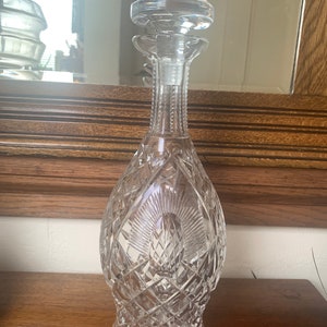 May include: A clear glass decanter with a cut crystal design and a stopper. The decanter has a tall, slender neck and a round body.